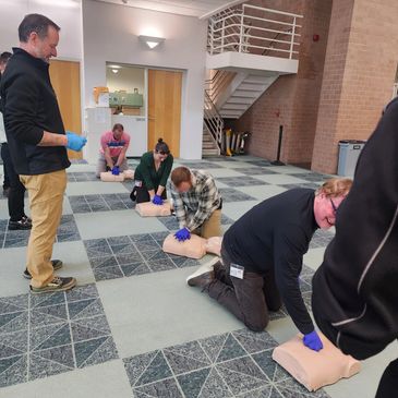 People practicing CPR on mannequins in a training session indoors.