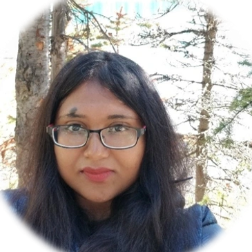 A woman with glasses and long hair outdoors among trees.