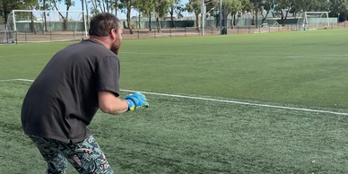 A man in gloves on a soccer field prepares to catch.