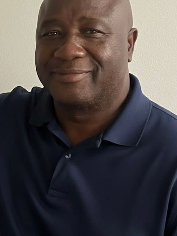 A man wearing a navy blue polo shirt smiling gently.