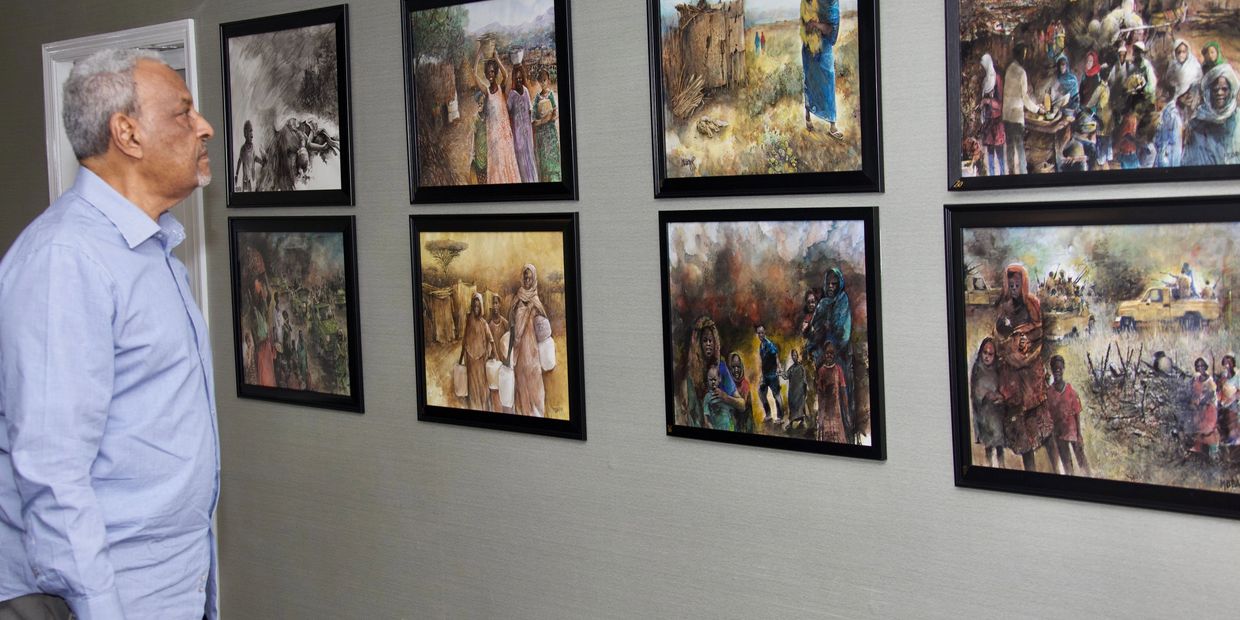 Man observing a wall of framed paintings depicting community life and struggles.