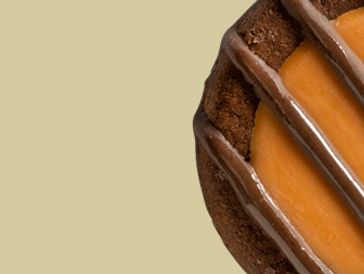 Close-up of a caramel-filled cookie with chocolate drizzle on a beige background.