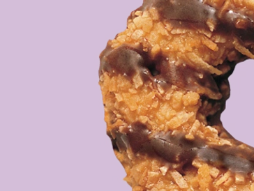 Close-up of a chocolate-drizzled coconut cookie on a purple background.