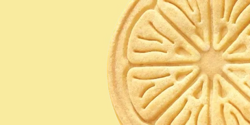 Close-up of a lemon-shaped cookie on a yellow background.