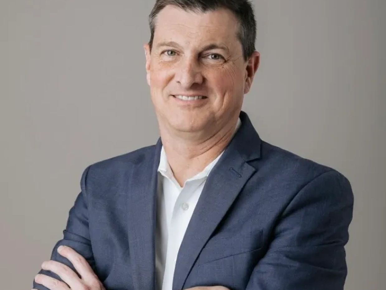 Confident man in blue suit with arms crossed smiling.