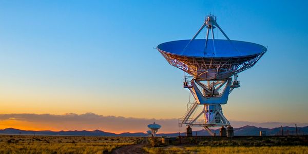 Large satellite dishes under a clear sky at sunset.