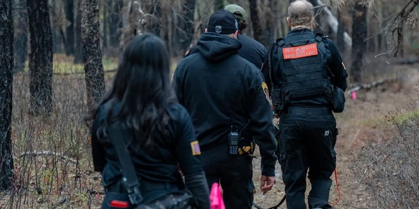 A group of search and rescue personnel walking through a wooded area.