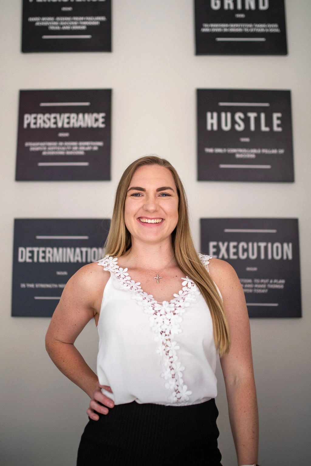 A smiling woman stands confidently in front of motivational wall art.