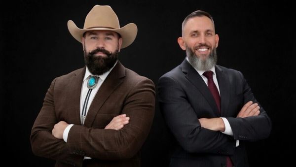 Two confident men in suits pose against a black background.