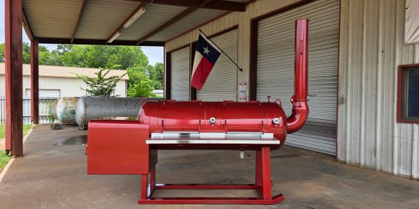 Red BBQ smoker grill under a covered area.