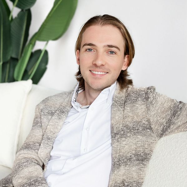 Young man in a textured jacket smiling on a white couch.