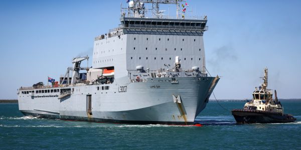 Large naval ship being guided by a tugboat.