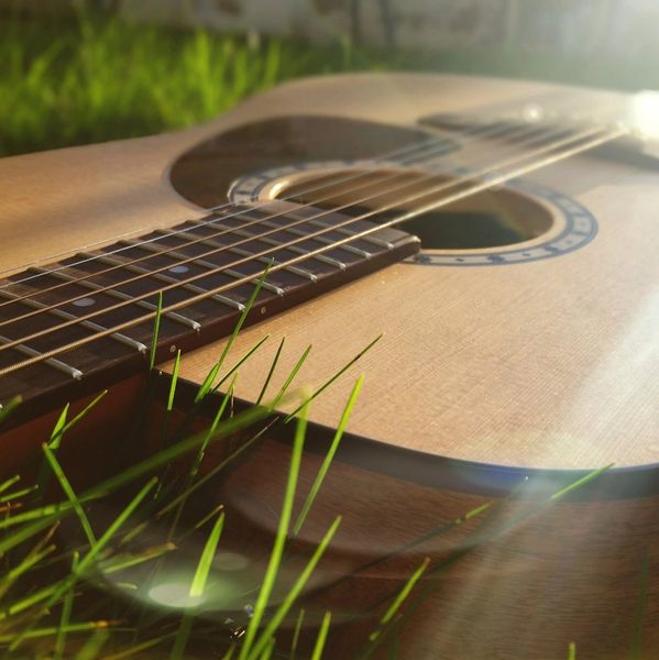 Close-up of an acoustic guitar lying on grass with sunlight shining on it.
