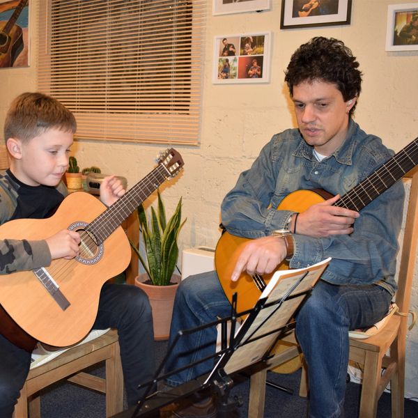 A man teaching a boy to play guitar indoors.