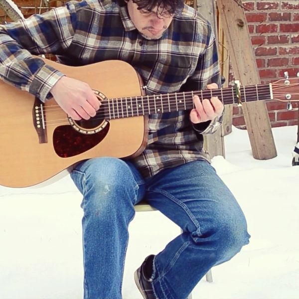 Man playing an acoustic guitar outdoors in the snow.