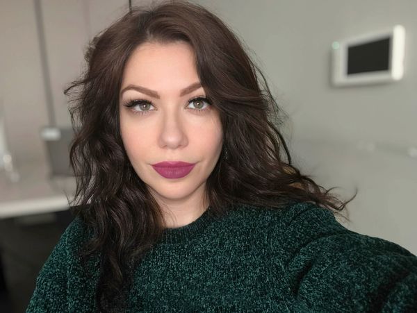Close-up selfie of a woman with dark curly hair and bold lipstick.