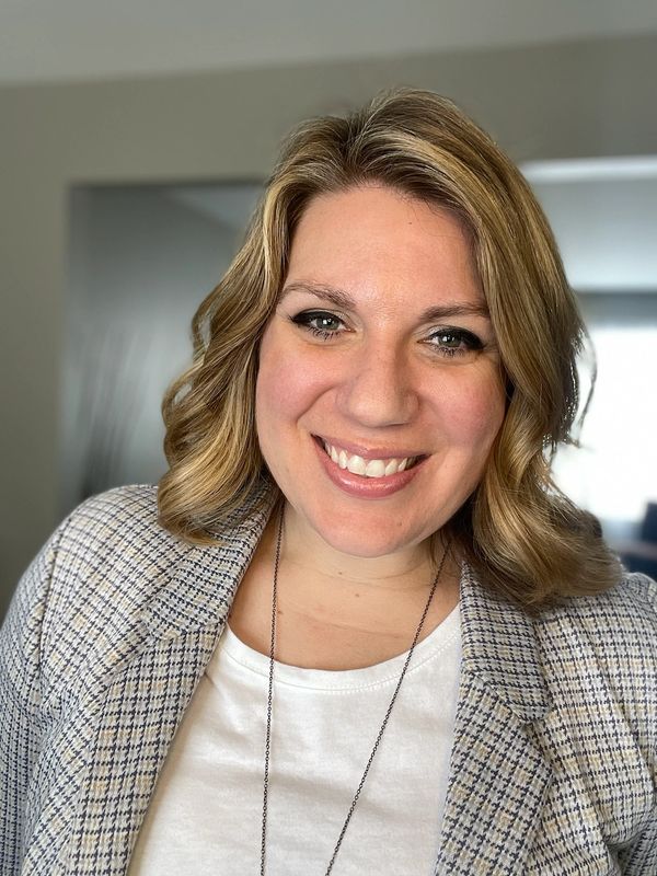 Smiling woman with blonde wavy hair in a checkered blazer.