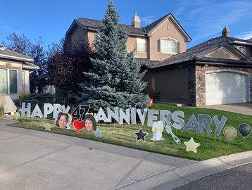 Custom yard sign celebrating a 47th anniversary with photo cutouts and festive decorations for an outdoor milestone event.