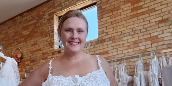 Smiling woman in a white lace dress inside a bridal shop.