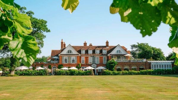 Large elegant brick mansion with manicured lawn and leafy trees.