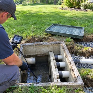Technician inspecting underground sewer distribution box with camera.