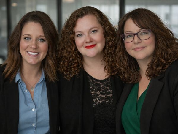 Three professional women smiling, dressed in business attire.