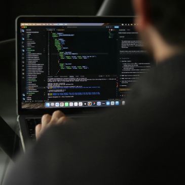 Person coding on a laptop with code visible on screen.