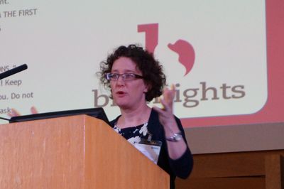 Woman speaking at a podium during a presentation.