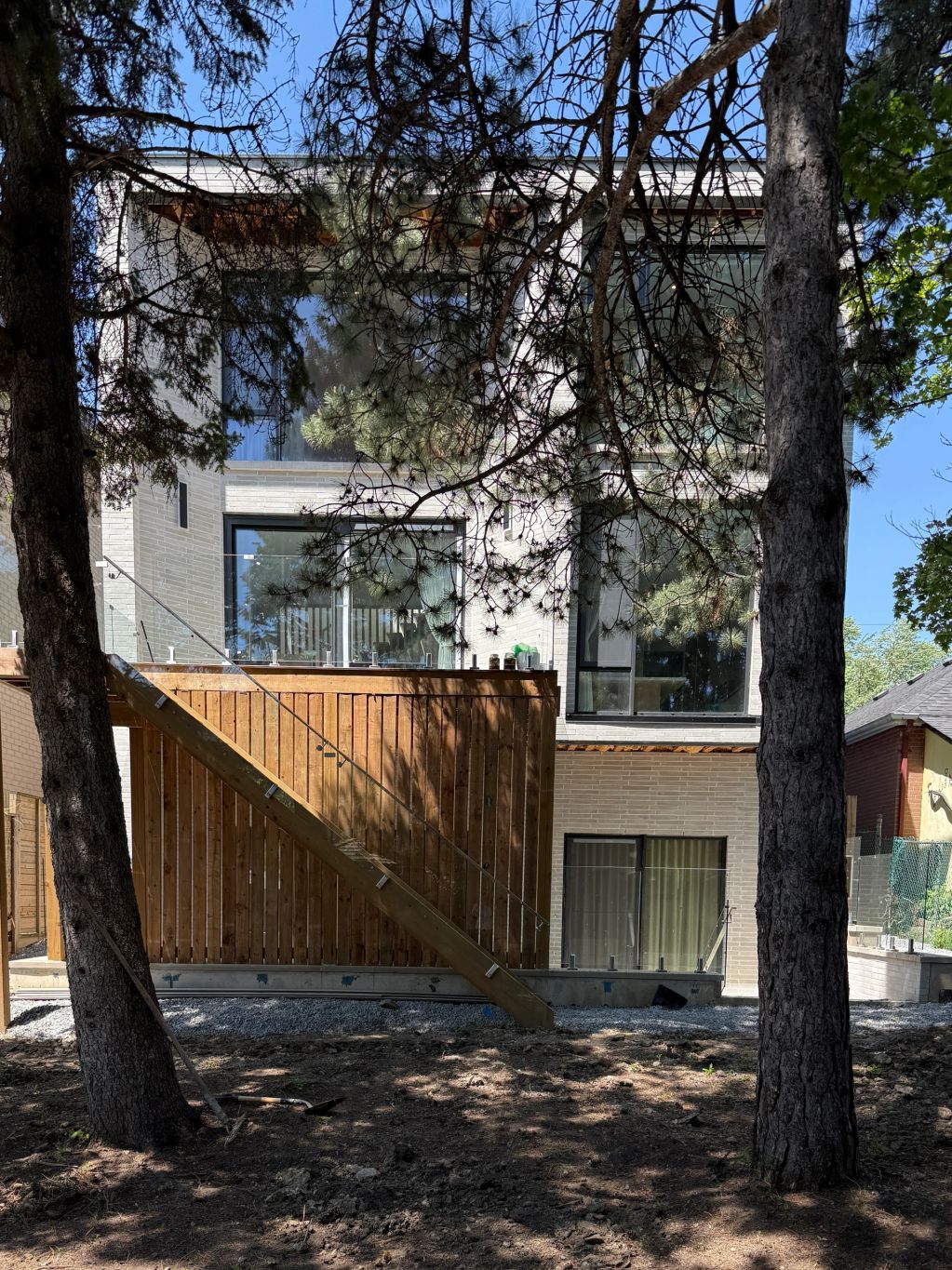 Modern house with wooden deck and staircase among tall trees.
