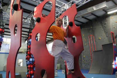Child climbing indoor rock wall with red panels.