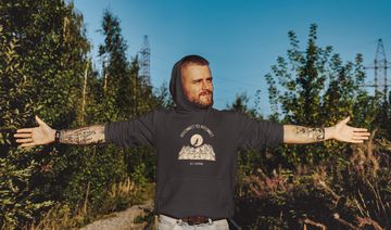 A man in the woods wearing a camping design hoodie.