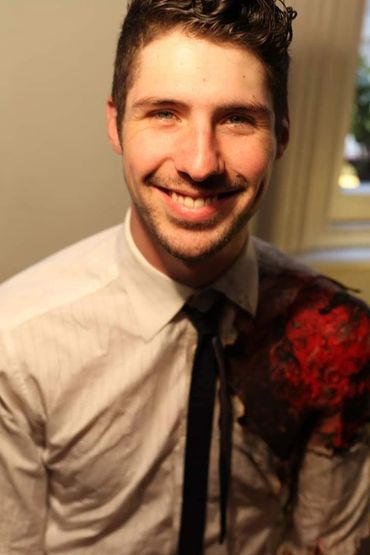 Smiling man in white shirt with artistic red and black design on shoulder.