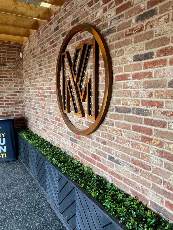 Photo of a corten laser cut MK logo in circle mounted on a brick wall