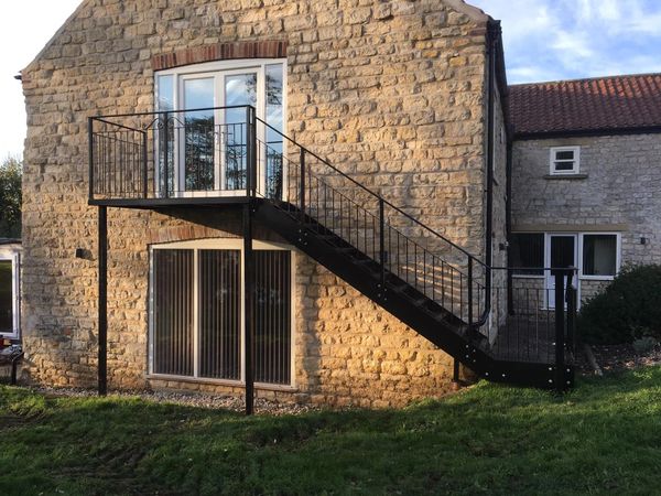 Black metal fire escape going up to a first floor door on the side of a limestone house.