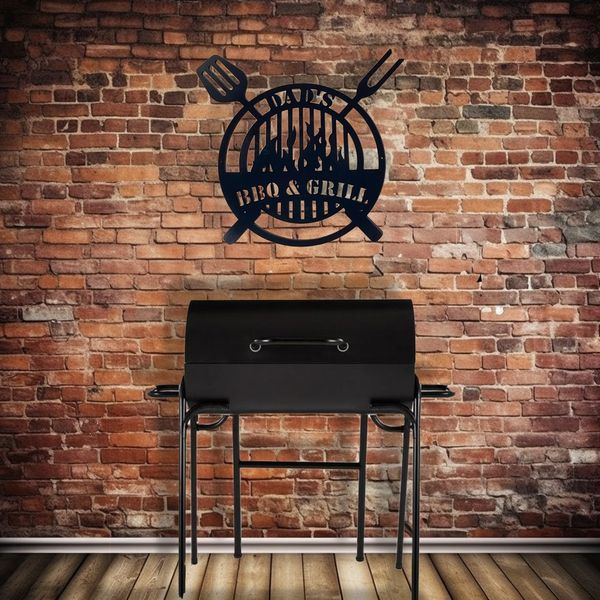 A photograph of a black metal laser cut BBQ griddle. The words DAD's BBQ & Grill are cut into the ar