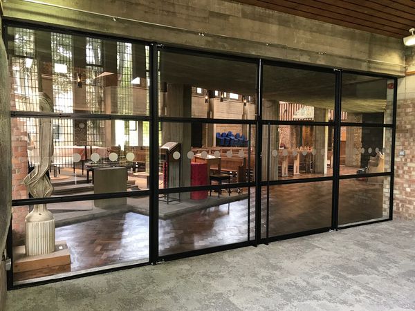 Photograph of glass panelled wall with double doors inside a church. glass panels are sectioned with