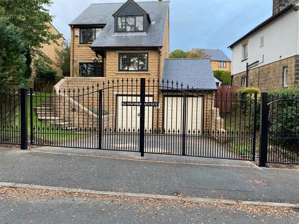 Photograph of large black bifold gates in front of a detached house.