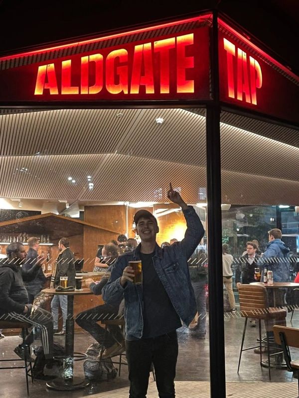 Photograph of a plasma cut sign above a window. The word Aldgate is lit up in red. There is a man un