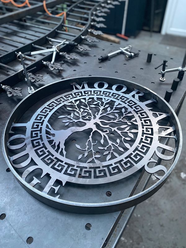 A photograph of a plasma cut metal fence centre piece. Circle shape with tree inside and the words M