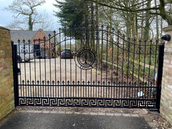 Photograph of black electric gate with bespoke tree logo in the centre.