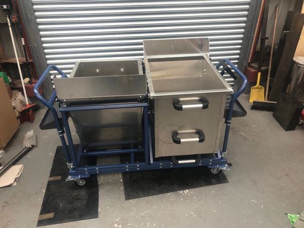 Photograph of a metal production delivery card on a blue frame with trolley wheels.