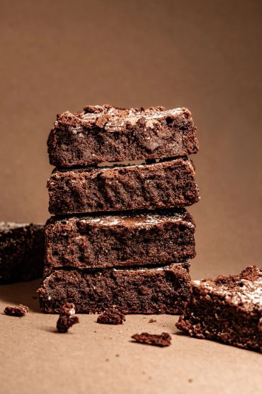 Stack of four chocolate brownies on a brown surface.