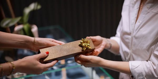 Two people exchange a gold gift box with a bow indoors.
