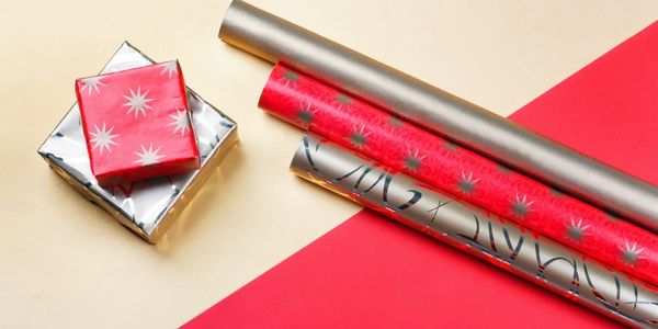 Two wrapped gifts and three rolls of festive wrapping paper on a beige and red surface.