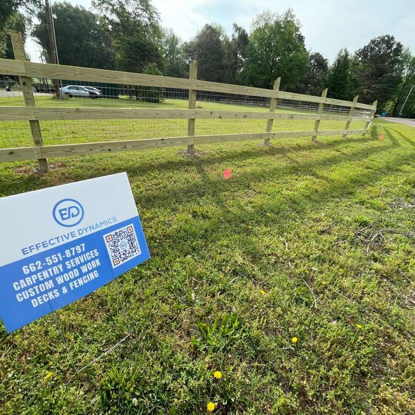 Freshly installed wooden fence with a carpentry service sign in a grassy area.
