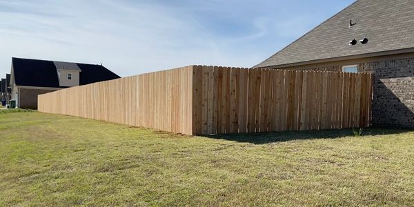 Long wooden fence surrounding a backyard of a house.