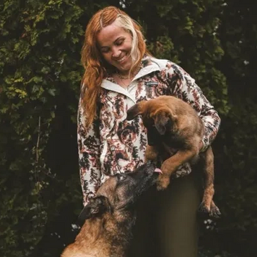 Woman holding a puppy while an adult dog interacts with them.