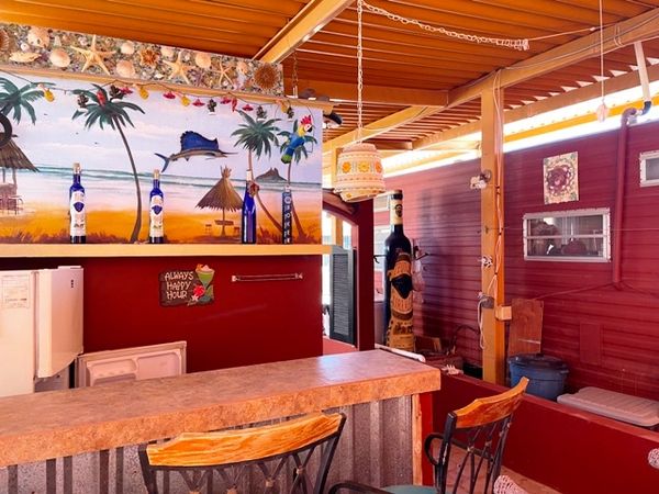 Cozy tropical-themed bar with wooden stools and vibrant wall art.