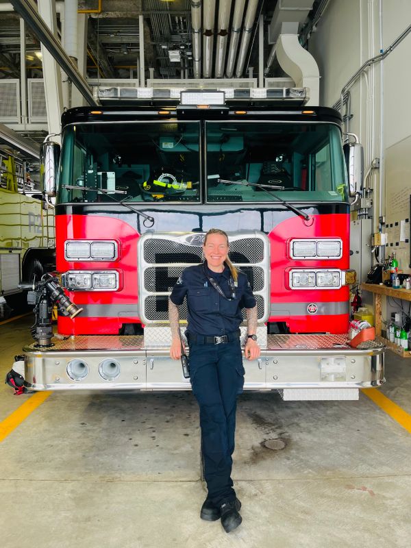 Firefighter smiling and posing in front of a fire truck.