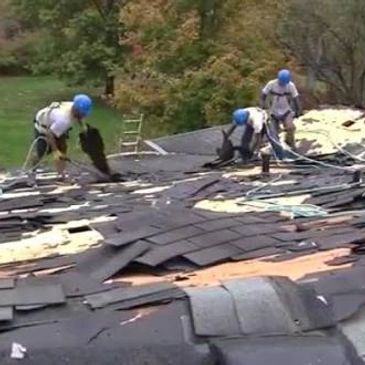Workers repairing a damaged roof with safety gear.